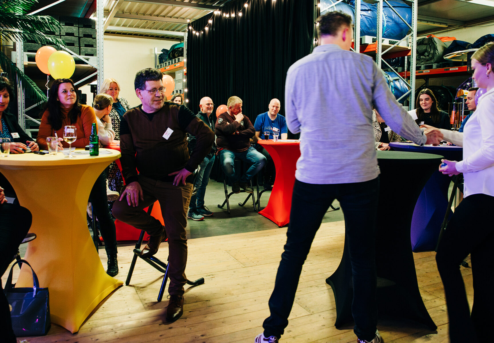 De Crazy Games worden gepresenteerd, de deelnemers kijken aandachtig toe.
