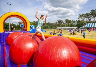 Deelnemer stapt van bal naar bal op de Stormbaan Mega Red Balls tijdens een zeskamp.