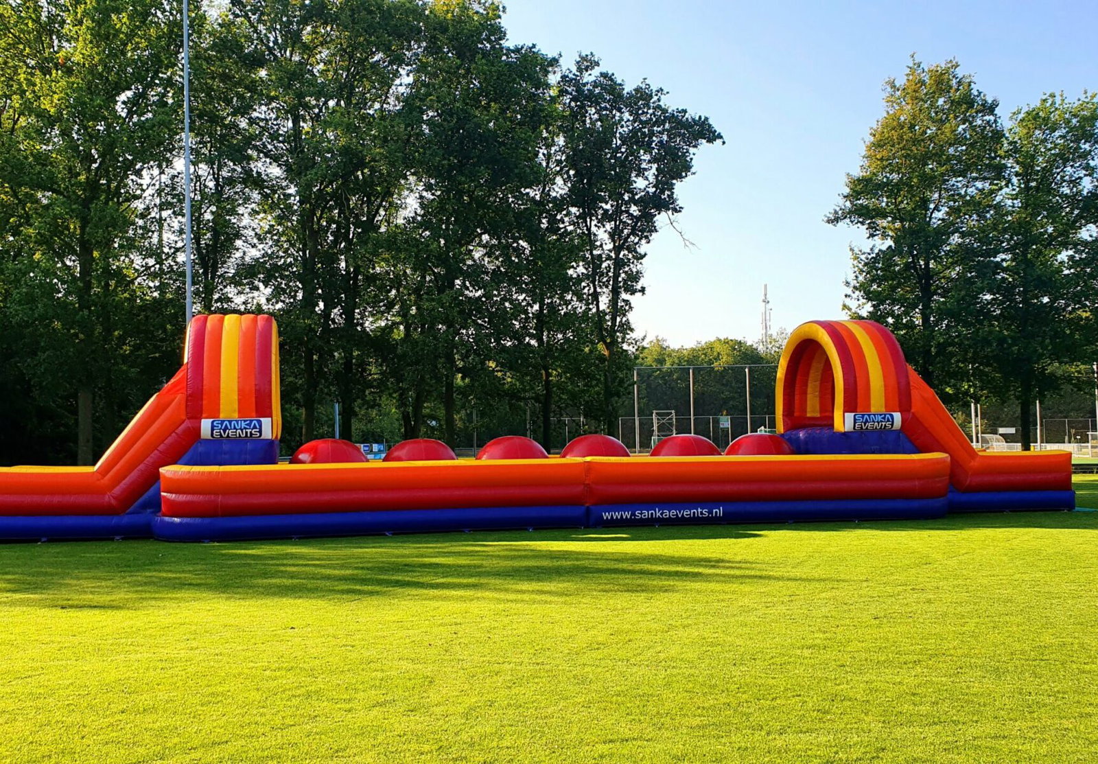 Zijaanzicht van de Stormbaan Mega Red Balls op een grasveld, met rode ballen tussen twee opblaasbare bogen.